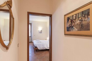 A hallway leading to a bedroom with a bed, a painting on the wall, and a mirror.