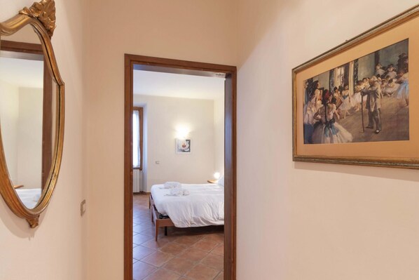 Un couloir menant à une chambre à coucher, où se trouvent un lit, un tableau accroché au mur et un miroir.