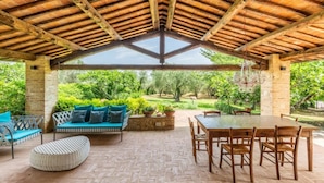 Une terrasse extérieure avec une table et des chaises en bois, un canapé avec des coussins et un banc en pierre.