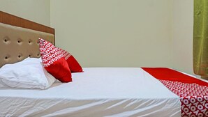 Un lit bien fait, recouvert d’une couvre-lit blanche et rouge à motifs, avec un oreiller blanc et un oreiller rouge orné d’un motif répété.