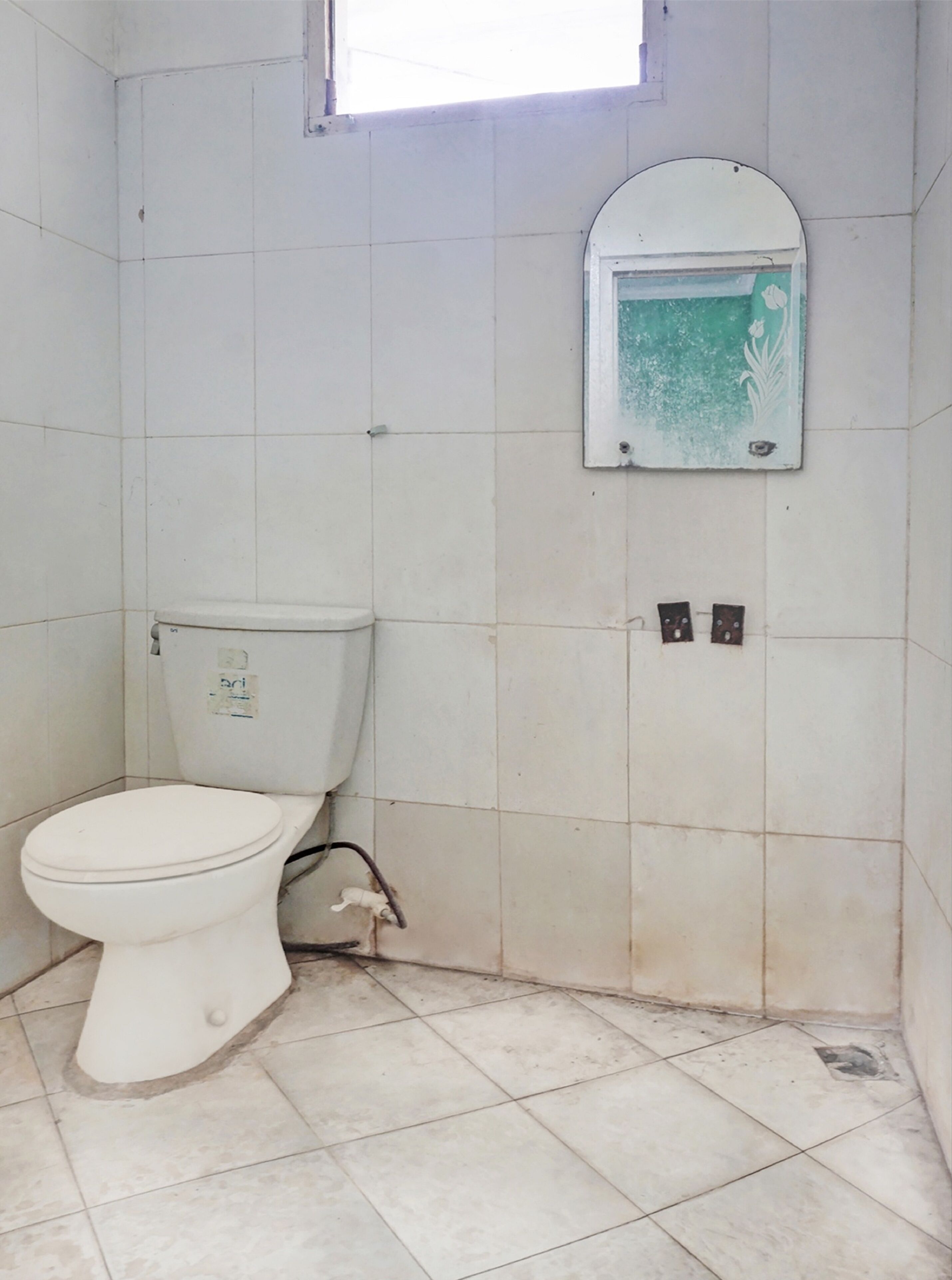 A small, tiled bathroom with a toilet, a wall-mounted sink, and a window above the sink.