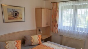 Une chambre à coucher comprenant un lit, des oreillers, une table de chevet, une armoire, un radiateur et une fenêtre avec des rideaux.