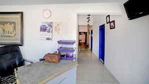 A hallway with a reception desk, a clock, and a blue door. - Hotel O Darussalam Inn (Medan)