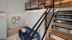 Una sala de estar moderna con un sofá azul, una mesa de centro y una escalera con barandilla negra.