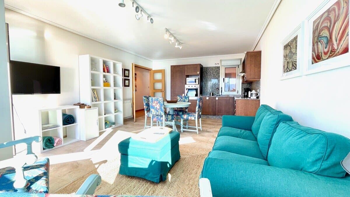 A living room with a teal sofa, a TV, and a dining area with chairs and a table.