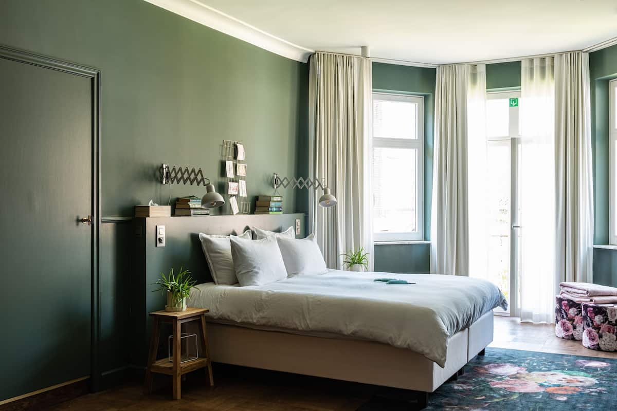 A neatly arranged bedroom with a bed, bedside tables, a small stool, and a window with curtains.
