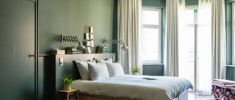 A neatly arranged bedroom with a bed, bedside tables, a small stool, and a window with curtains.
