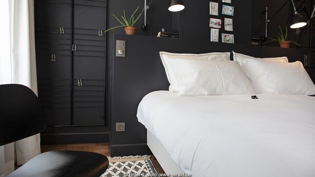 A modern bedroom with a black wardrobe, a bed with white bedding, and multiple wall-mounted lamps. - BROEL4 (Kortrijk)