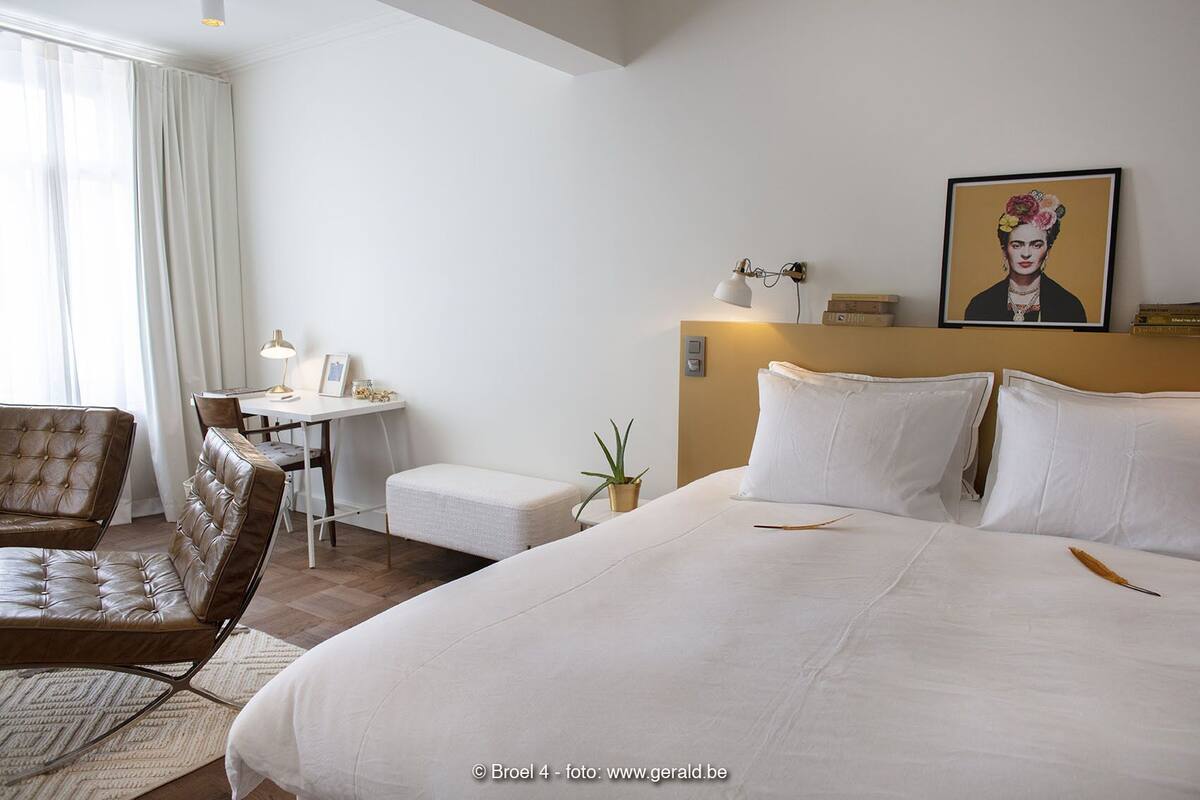 A hotel room with a large bed, a desk, a chair, and a painting on the wall.