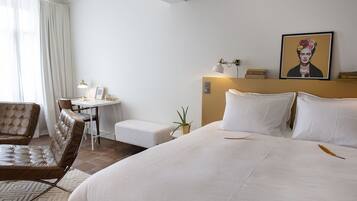 A hotel room with a large bed, a desk, a chair, and a painting on the wall.