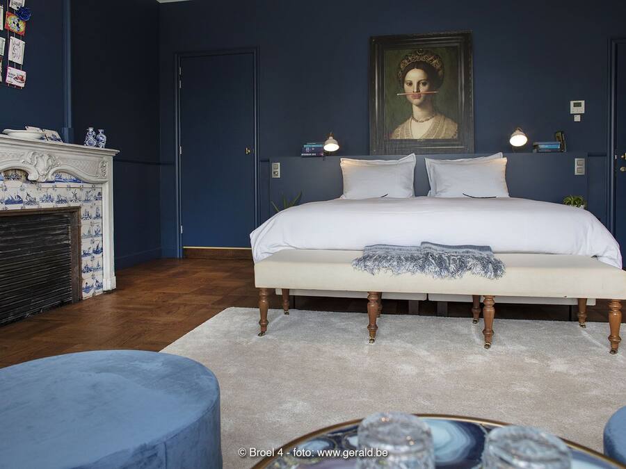 A bedroom with a large bed, a fireplace, and a portrait on the wall.