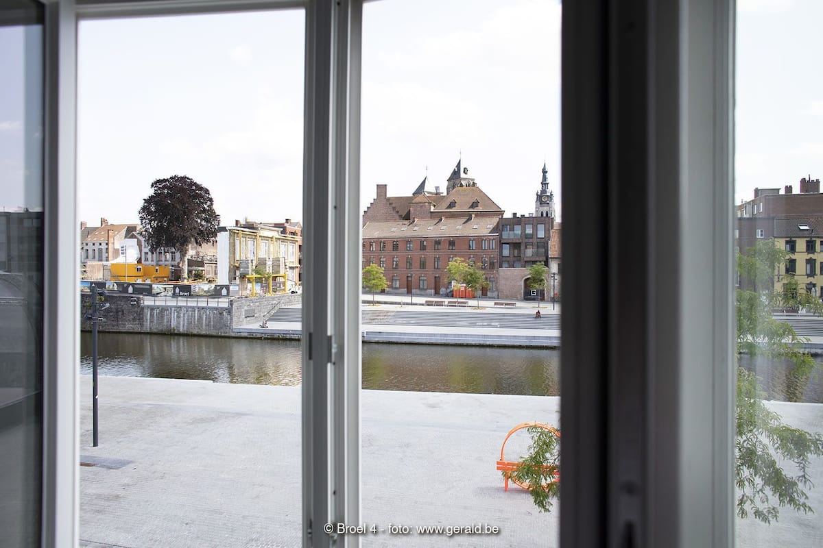 A view through a window of a building with a river in the foreground, a bridge, and buildings with distinct architectural styles in the background.