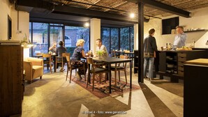 A modern dining area with exposed brick ceilings, large windows, and a mix of wooden and metal furniture. - BROEL4 (Kortrijk)