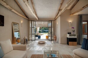 Een moderne woonkamer met een glazen deur die leidt naar een terras, een bank, een salontafel en een bijzettafeltje met een lamp.