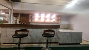 A bar area with two stools, a marble countertop, and a shelf with bottles and glasses. - MeroStay 025 Atithi Satkar (Mahamanjushree Nagarkot)