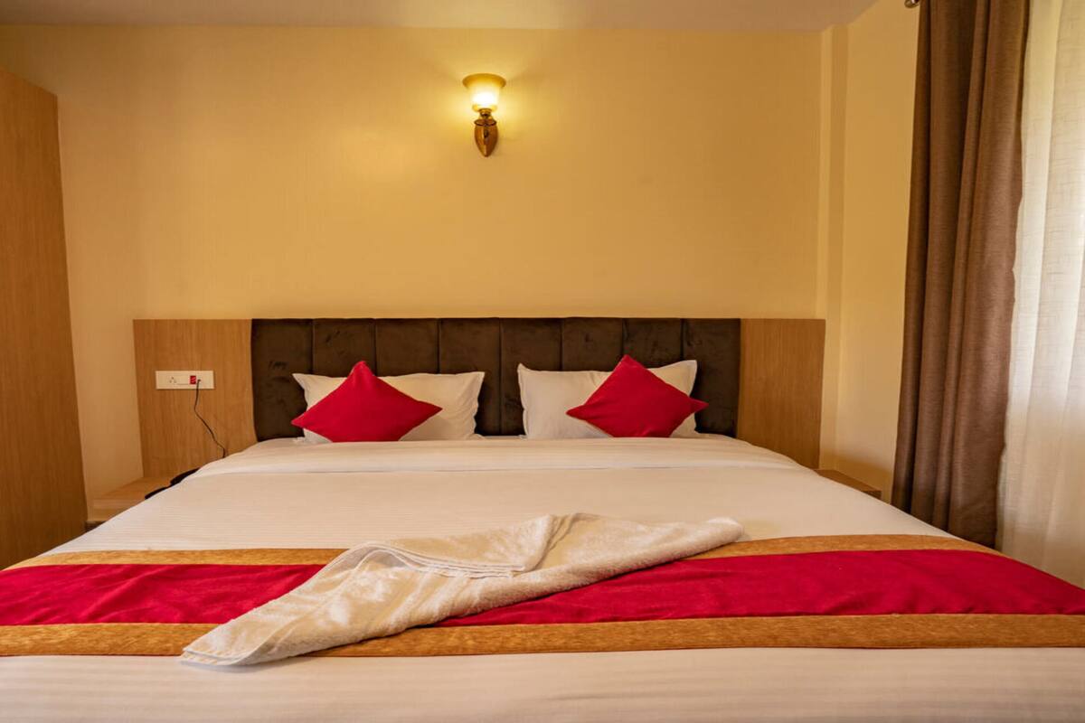 A hotel room with a large bed, a wooden wardrobe, and a wall-mounted light fixture.