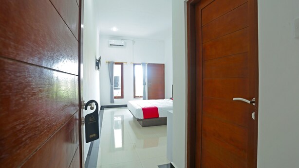 A hotel room with a bed, a wooden door, and a hallway leading to another room. - OYO 90859 Cahaya Guest House (Denpasar)