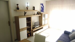 Een woonkamer met een houten tv-meubel, een bank en een eettafel.