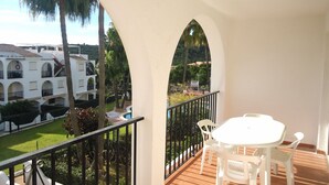 Een balkon met een witte tafel en stoelen, een zwembad en uitzicht op een gebouw met bogen.