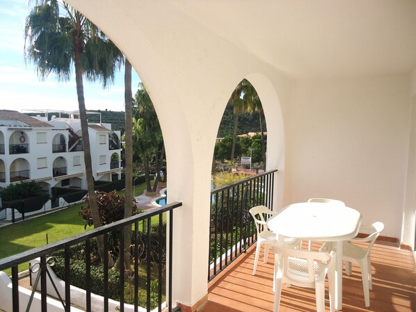 Un balcón con una mesa y sillas blancas, una piscina y vistas a un edificio blanco con arcos.