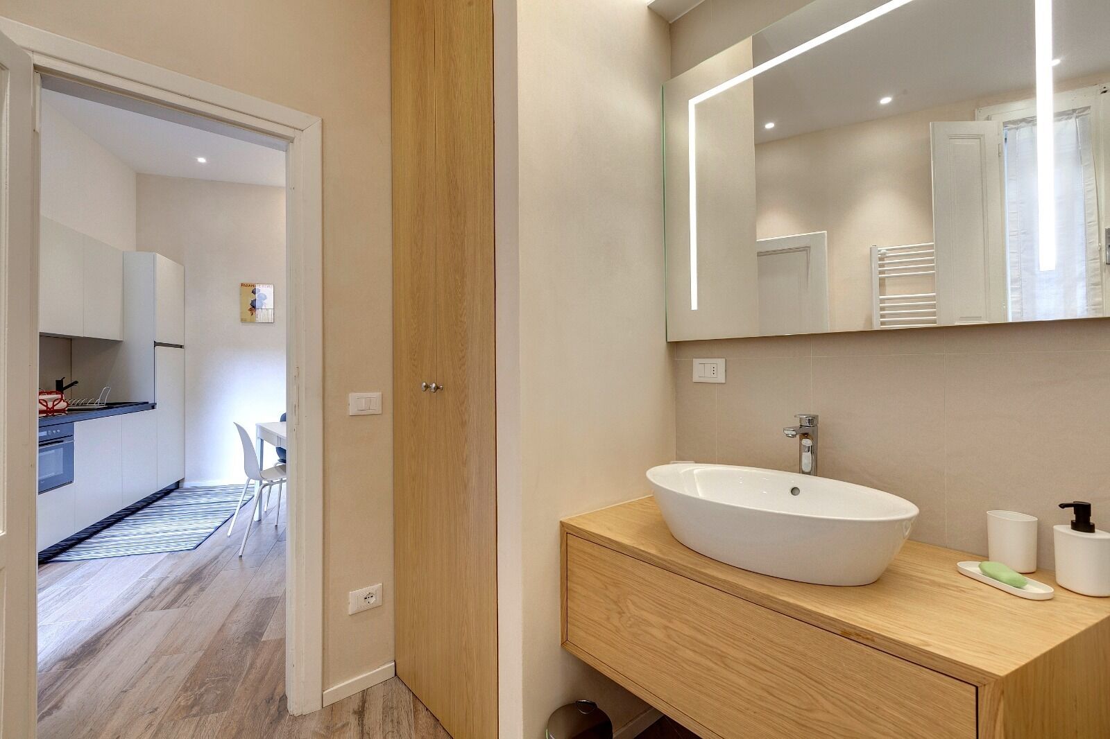 A modern bathroom with a large mirror, a white sink, and a wooden vanity.