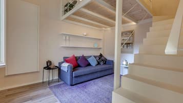 Ein modernes Wohnzimmer mit einem blauen Sofa, einem gemusterten Teppich und einer Treppe zu einer oberen Etage.
