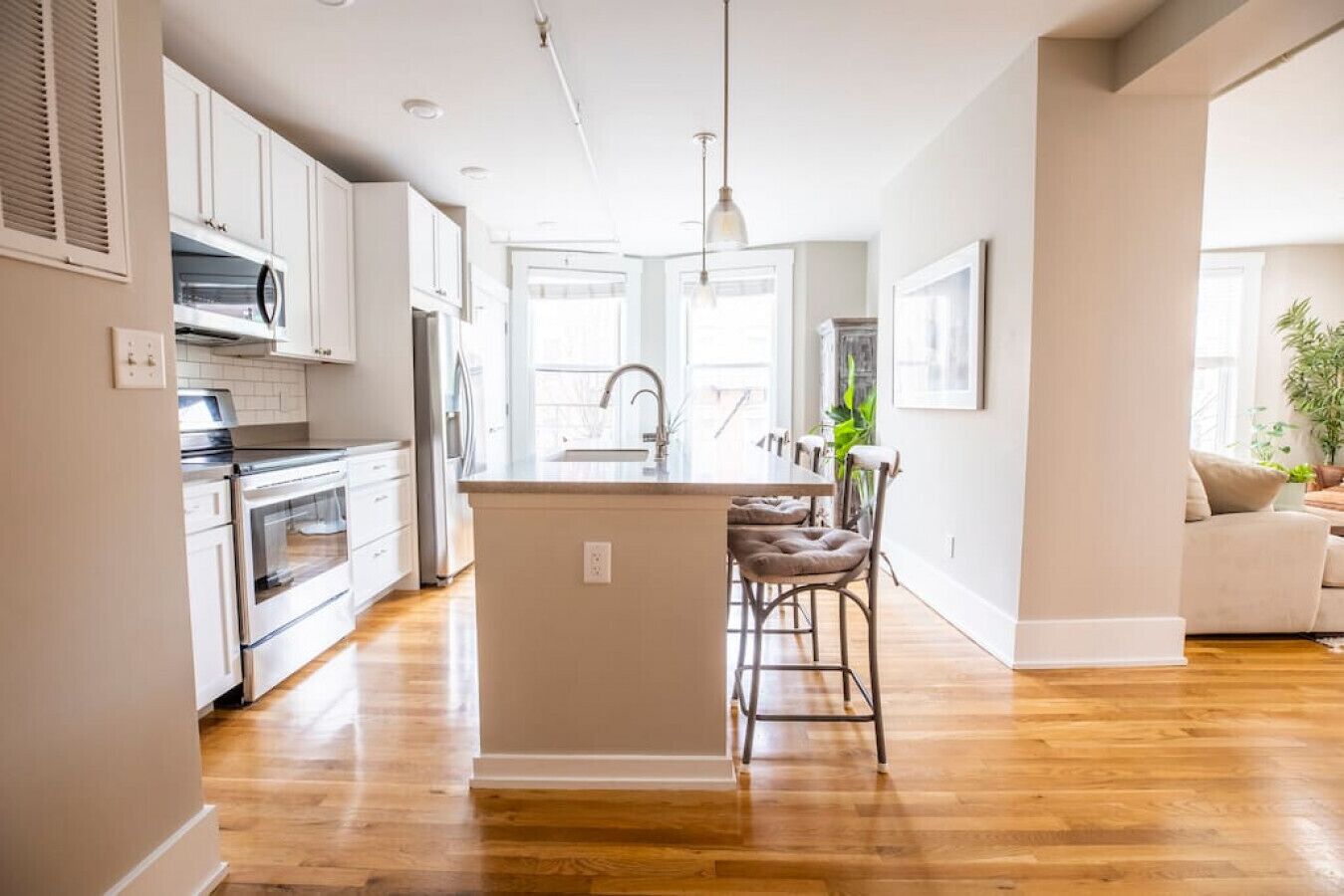 Una cocina moderna con armarios blancos, una isla central y una zona de comedor con un taburete de bar.