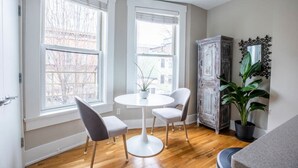 A room with a round white table, two white chairs, a potted plant, a wooden cabinet, and a mirror on the wall. - Lux Condo in the Heart of OTR | Walk Everywhere (Cincinnati)