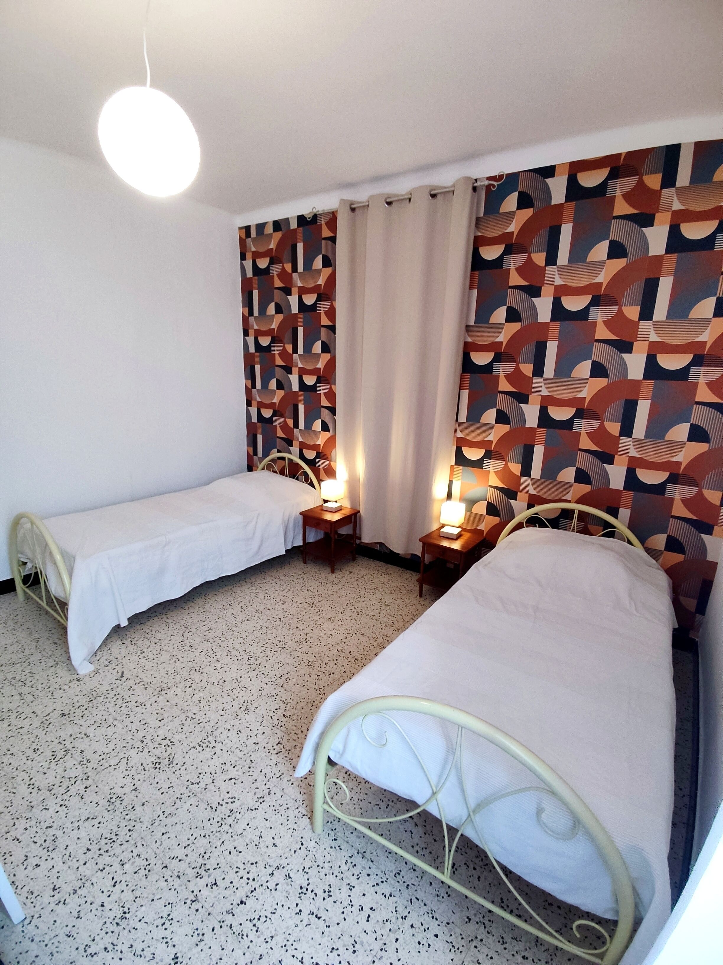 Une chambre avec deux lits simples, un mur orné d’un motif, un luminaire au plafond et un sol à motifs.