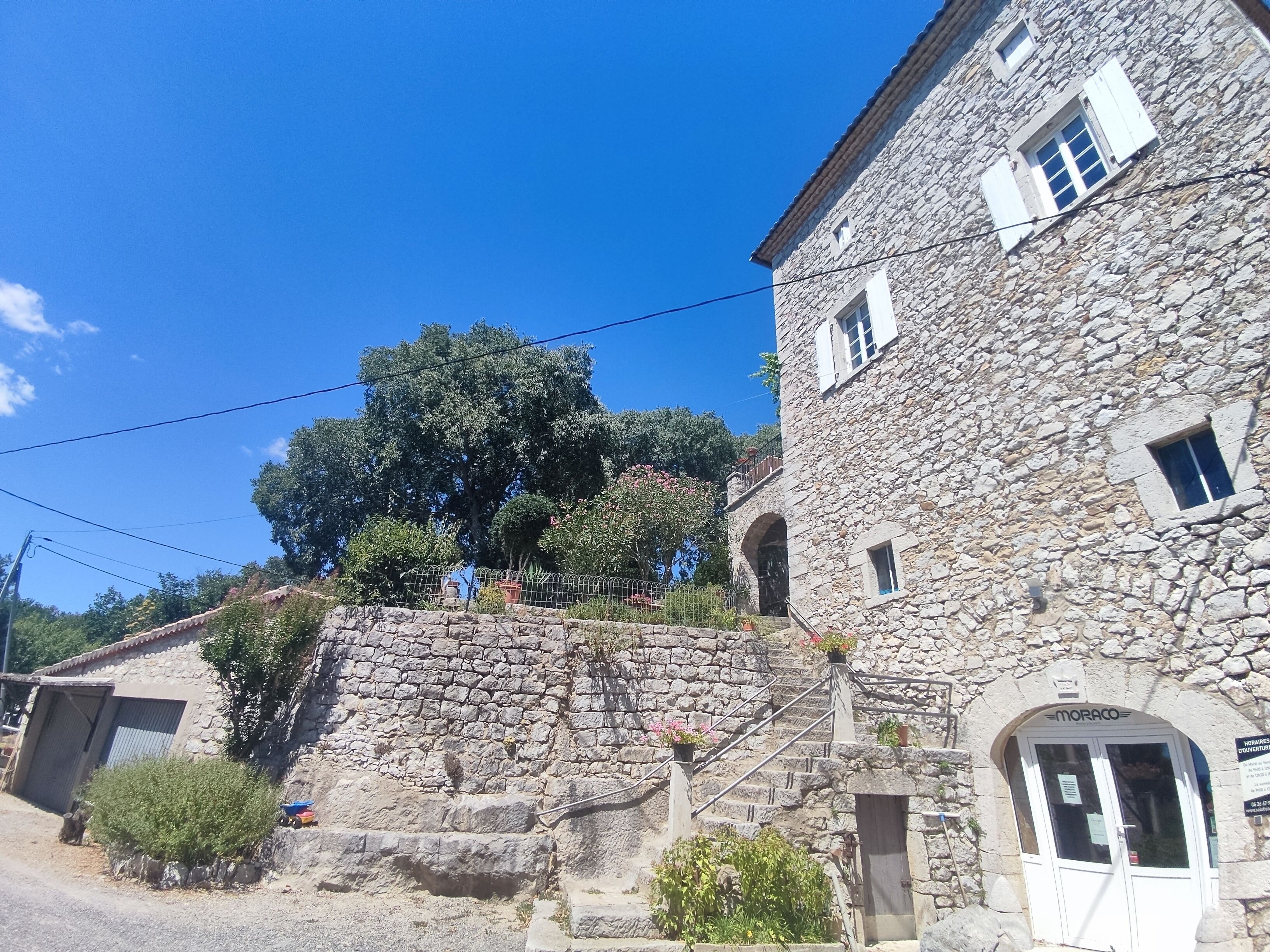 A stone building with a staircase leading to an upper level, a door labeled "MORACO," and a small balcony.