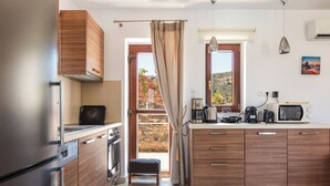 A modern kitchen with wooden cabinets, stainless steel appliances, and a view of the outdoors through a large window. - Sea views, short drive to the beach and shops! (Agios Nikolaos)