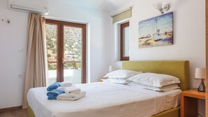 A hotel room with a bed, a window with curtains, a painting on the wall, and an air conditioning unit. - Sea views, short drive to the beach and shops! (Agios Nikolaos)