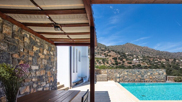 Un espacio al aire libre cubierto con piscina, muros de piedra y vistas a un paisaje montañoso.