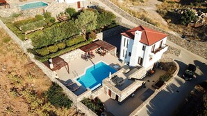 Un edificio de dos pisos con piscina, mobiliario exterior y un muro de piedra que rodea la propiedad.