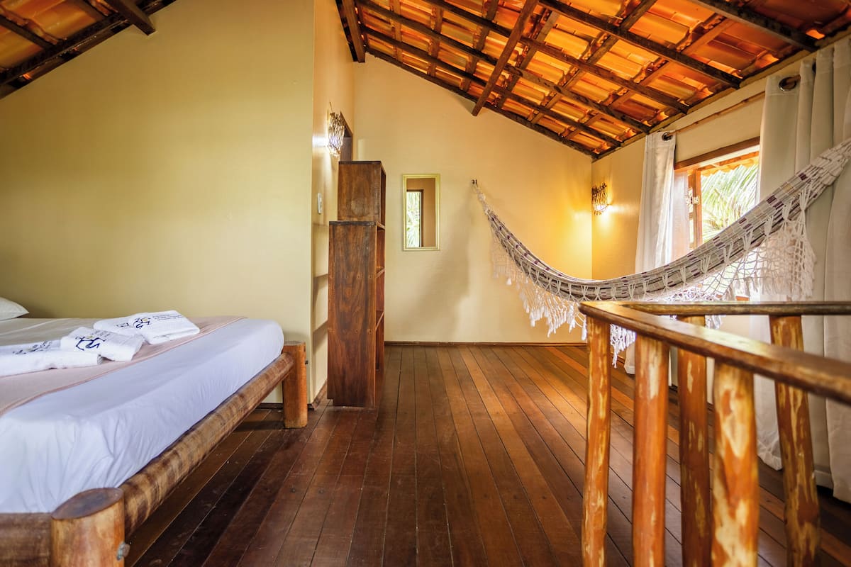 A room with a wooden bed, a hammock, and a wooden floor.