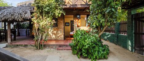 A rustic building with a wooden balcony, a thatched roof structure, and a paved courtyard.