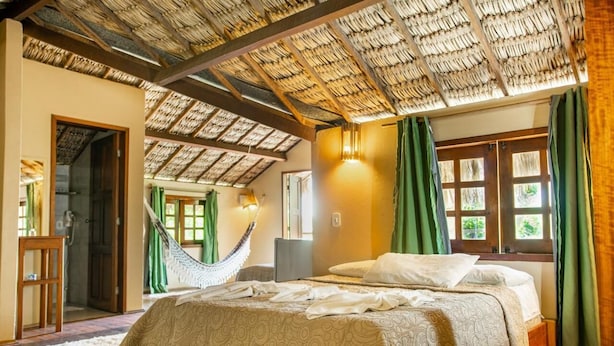 Een kamer met een bed, een hangmat, een bureau en een raam met gordijnen.