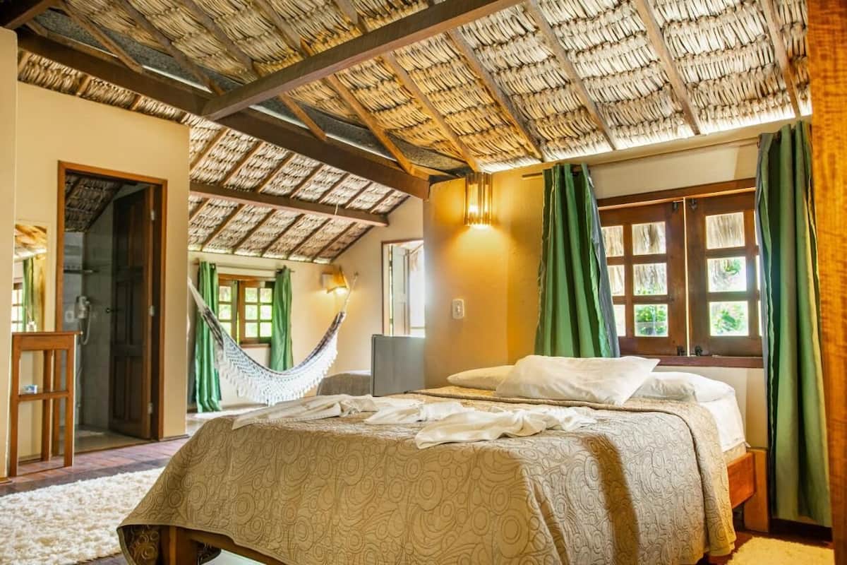 A room with a bed, a hammock, a desk, and a window with curtains.