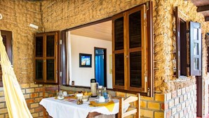 Een rustieke eetruimte met een tafel voor twee personen, een bakstenen muur en houten luiken.