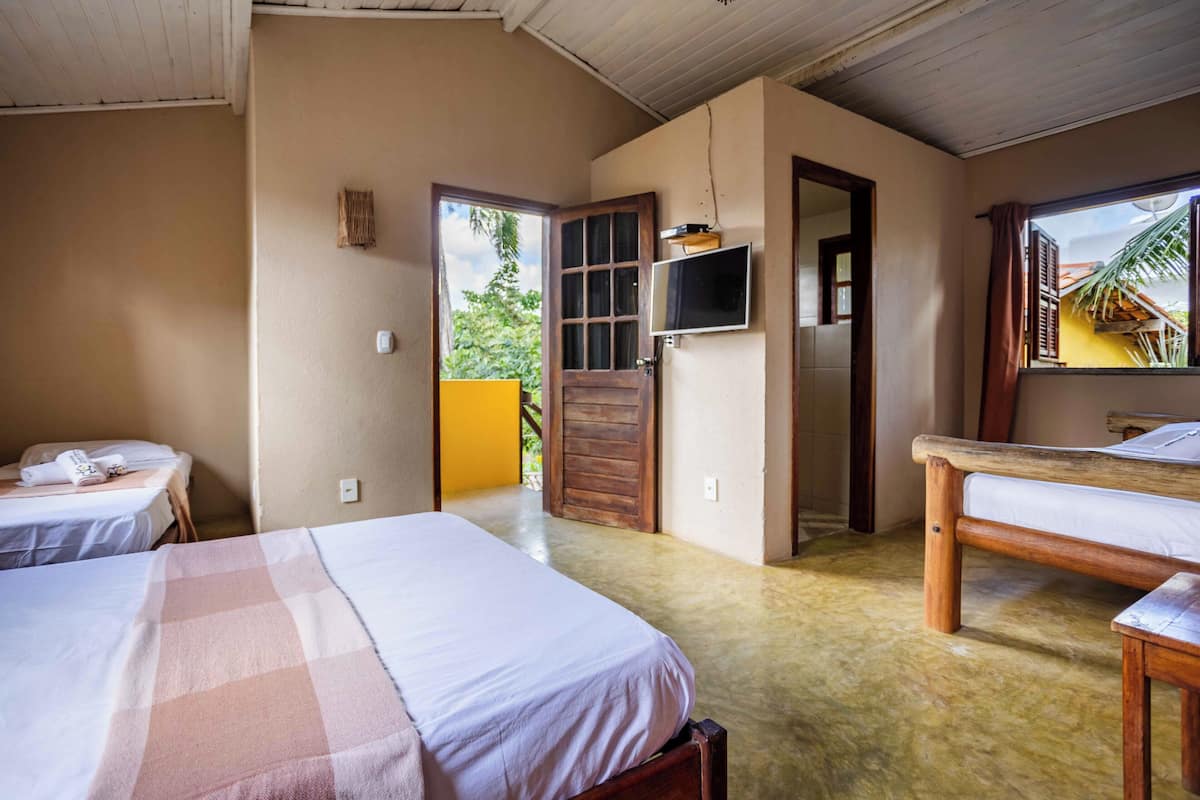 A room with two beds, a wooden table, a television, and a door leading outside.