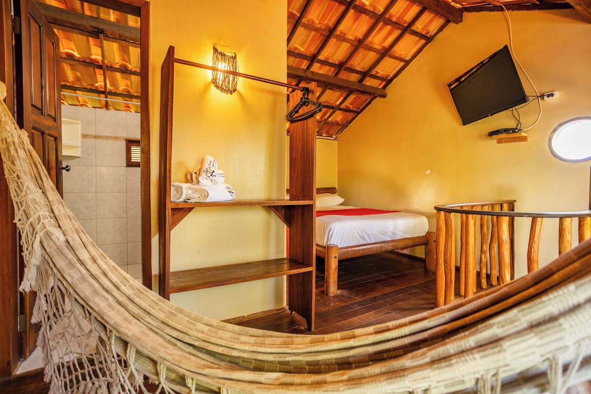 A hammock in a room with a bed, wooden shelves, a mounted TV, and a small round window.