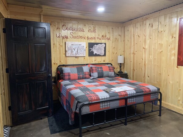 Une pièce chaleureuse avec un mur en bois, un lit recouvert d’une courtepointe, une porte et une carte accrochée au mur.