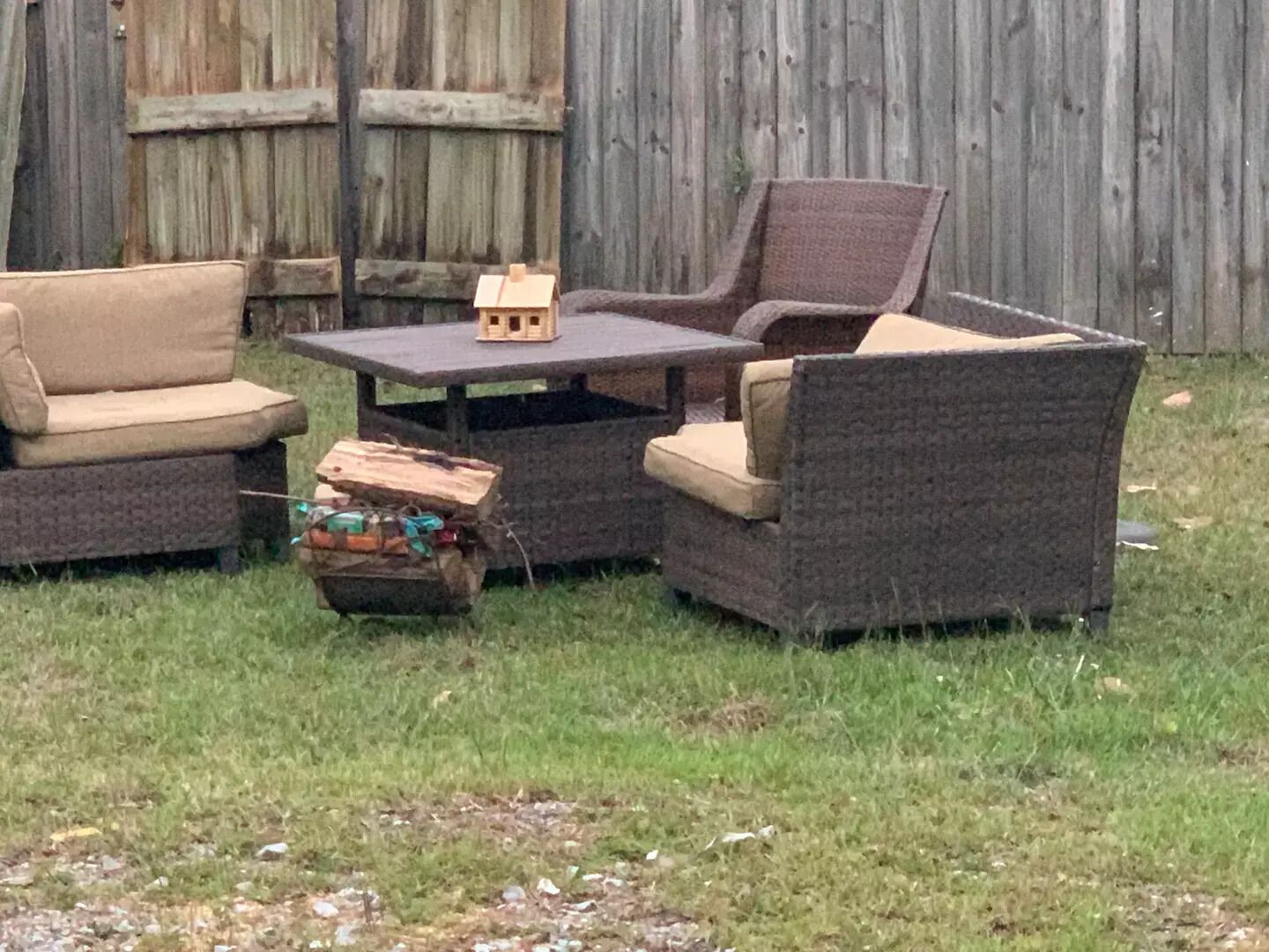 An outdoor seating area with wicker furniture and a small wooden house model on a table.