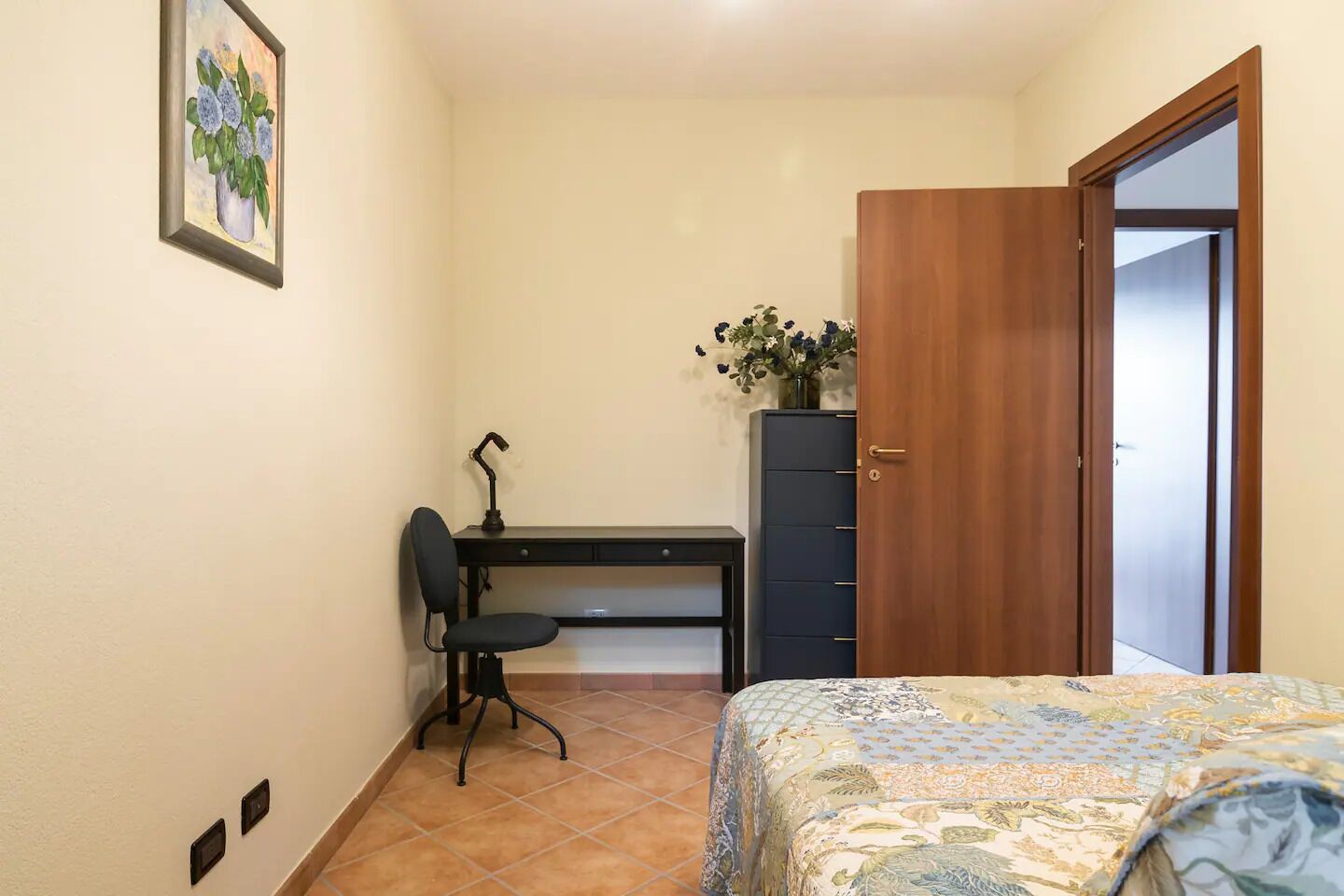Een slaapkamer met een bed, een bureau met stoel, een kledingkast en een deur.