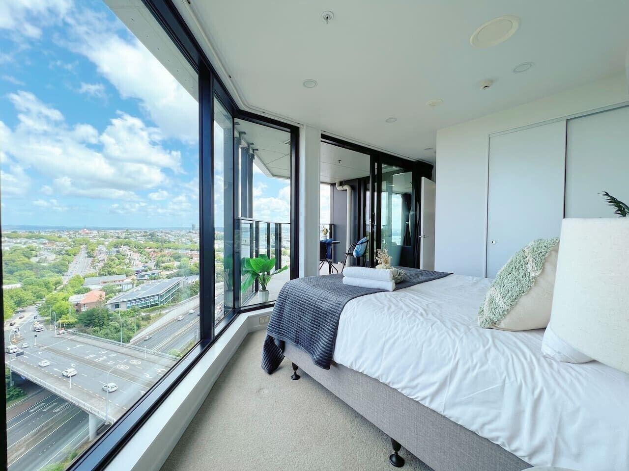 Une chambre moderne avec une grande fenêtre, un lit et une vue sur le paysage urbain.