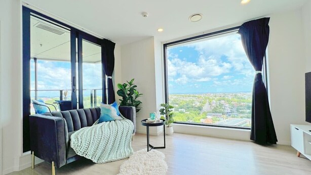 Una sala de estar moderna con un sofá, una mesita auxiliar, una planta en maceta y vistas de la ciudad.