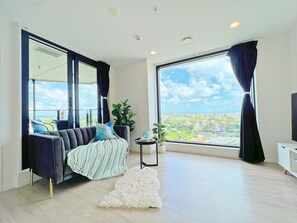 A modern living room with a sofa, a small side table, a potted plant, and a view of the city.