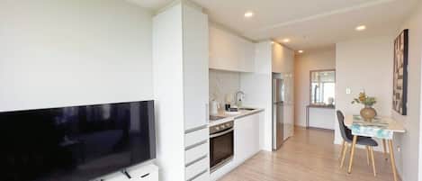 Una cocina moderna con armarios blancos, horno empotrado y comedor con mesa y sillas.