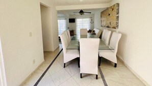 A spacious dining area with a glass table and white chairs, a ceiling fan, and a painting on the wall. - Nice house in front of the beach, in Acapulco Diamante (Acapulco de Juárez)