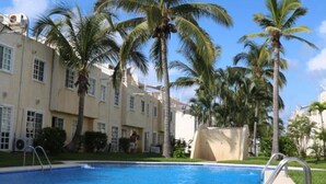 A swimming pool with clear blue water, surrounded by palm trees and a building with multiple windows. - Nice house in front of the beach, in Acapulco Diamante (Acapulco de Juárez)